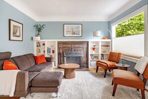 Uma sala de estar com lareira, um sofá, uma poltrona e uma mesa de centro.