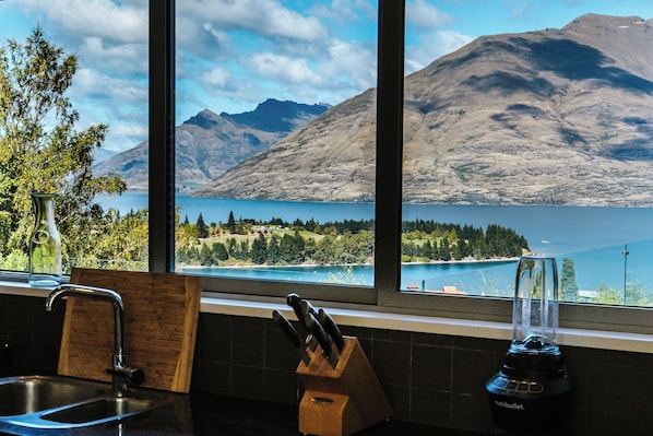 Una cocina con pileta, bloque de cuchillos y licuadora, con vista a un lago y montañas.