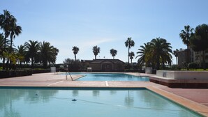 A swimming pool with palm trees, a building in the background, and a clear sky. - Alcaudón 86 - Two Bedroom Apartment, Sleeps 4 (Punta del moral)