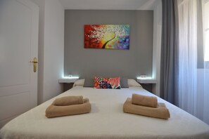 A hotel room with a bed, two towels, a colorful painting on the wall, and a window with curtains. - Alcaudón 86 - Two Bedroom Apartment, Sleeps 4 (Punta del moral)