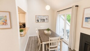 A dining area with a wooden table and white chairs, a painting above the table, and a fireplace on the right. - Upscale Rehoboth Retreat Minutes from Beach & Boardwalk (Rehoboth Beach)