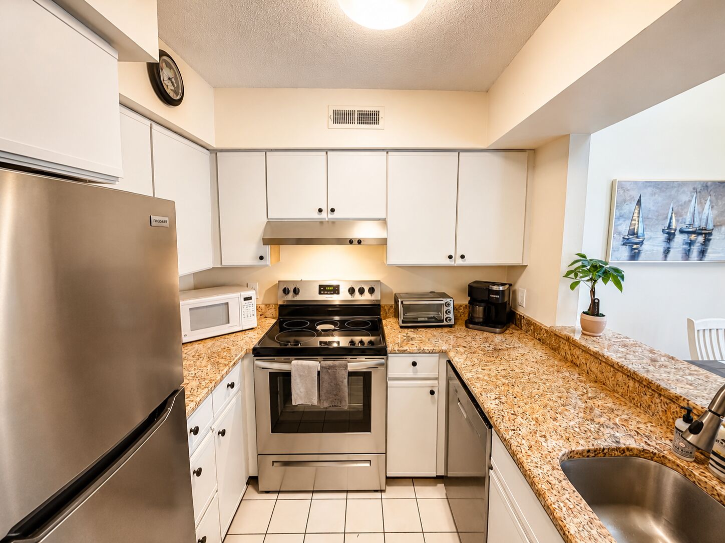 A kitchen with white cabinets, a stainless steel refrigerator, a microwave, a stove, a toaster, and a coffee maker.