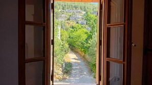 Une porte ouverte donnant sur un sentier bordé de verdure et flanqué de bâtiments en pierre.