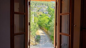 An open door leading to a pathway surrounded by greenery and stone buildings.