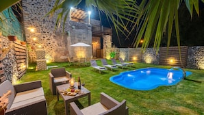 Un jardin avec une piscine, des chaises longues, une table avec des collations et un mur en pierre.