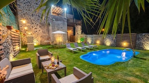 A backyard with a swimming pool, lounge chairs, a table with snacks, and a stone wall.