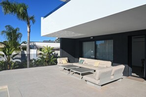 Ein moderner Außenbereich mit einer Sofagarnitur und Couchtisch, umgeben von einer Pflasterterrasse mit Pflanzen.