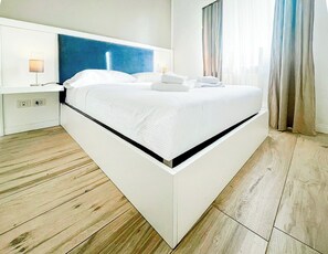 Ein modernes Hotelzimmer mit einem großen Bett, einem Kopfteil, Nachttischlampen und Blick auf die Stadt durch das Fenster.