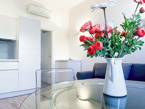 Ein modernes Wohnzimmer mit einem Glastisch, einer weißen Vase mit Blumen und einem Sofa.