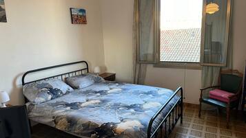 A bedroom with a bed, a chair, a window, and a picture on the wall.