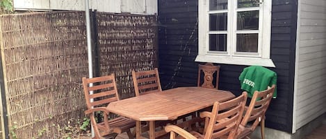 A wooden deck with a table and chairs, a window, and a covered area with a bamboo fence.
