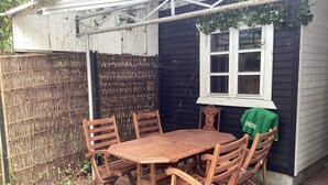 A wooden deck with a table and chairs, a window, and a covered area with a bamboo fence. - 6 Person Holiday Home in Vaeggerlose (Vaeggerlose)