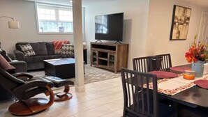 Uma sala de estar com sofá, televisão, mesa de jantar com cadeiras e mesa de centro.