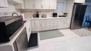 Uma cozinha moderna com armários brancos, micro-ondas, cafeteira e geladeira.