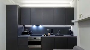 Eine moderne Küche mit dunklen Schränken, einem Einbauofen, einer Spüle und einer Arbeitsplatte mit Wasserkocher und weiteren Küchengeräten.