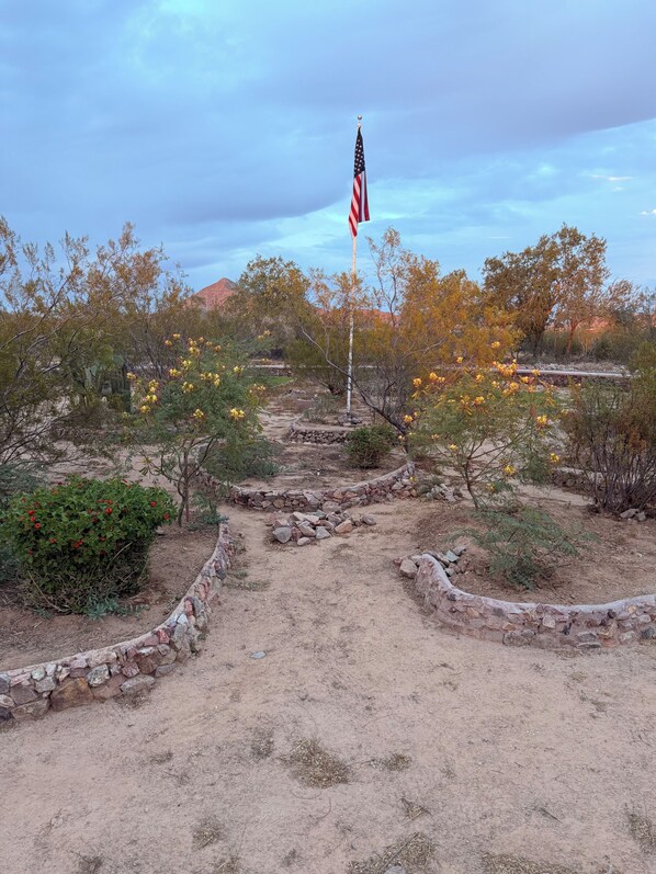 A flagpole with an American flag, surrounded by desert vegetation and a stone pathway.