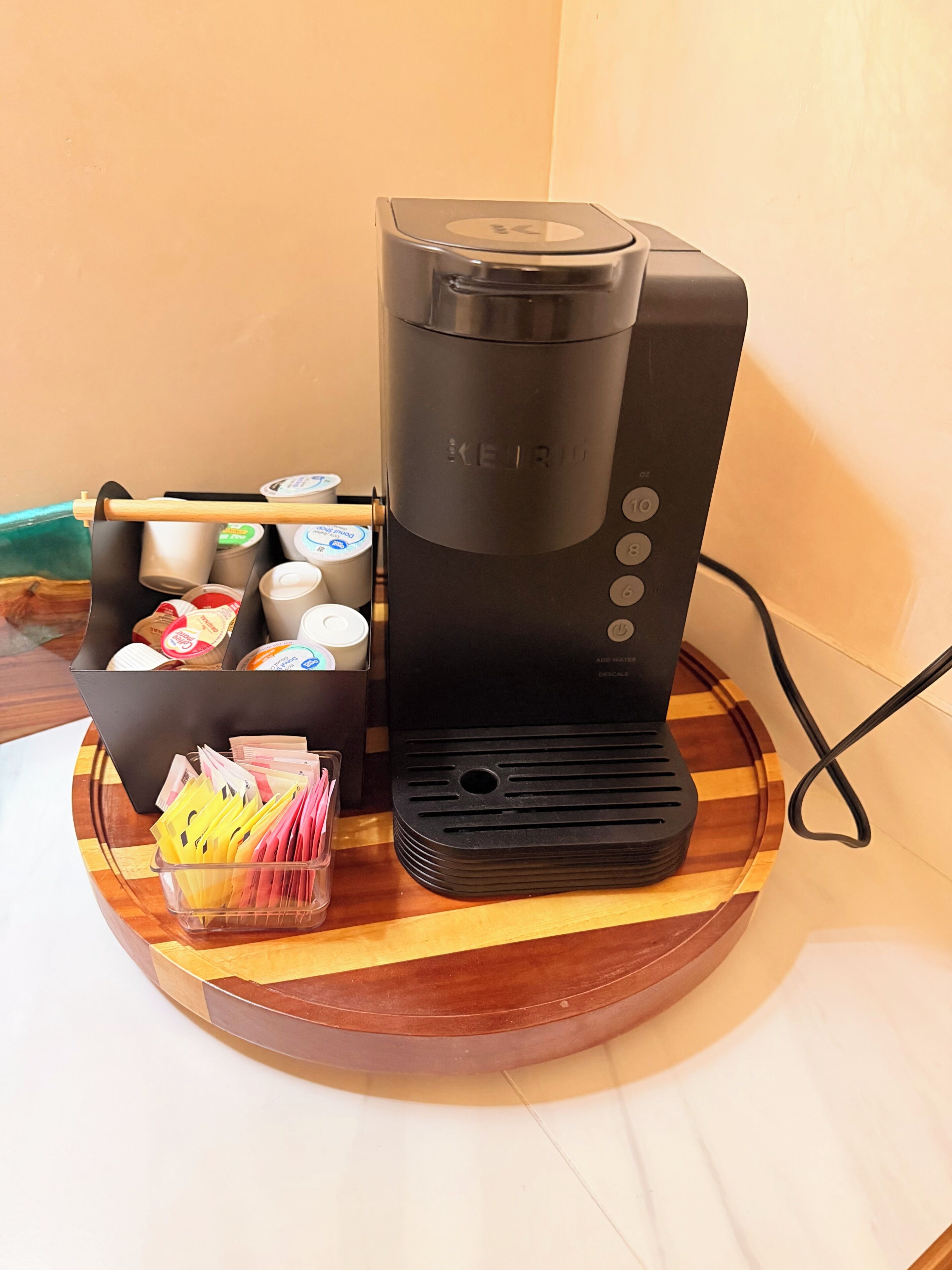 Une machine à café Keurig posée sur un plateau en bois, avec un support pour les dosettes de café et un récipient rempli de serviettes en papier.