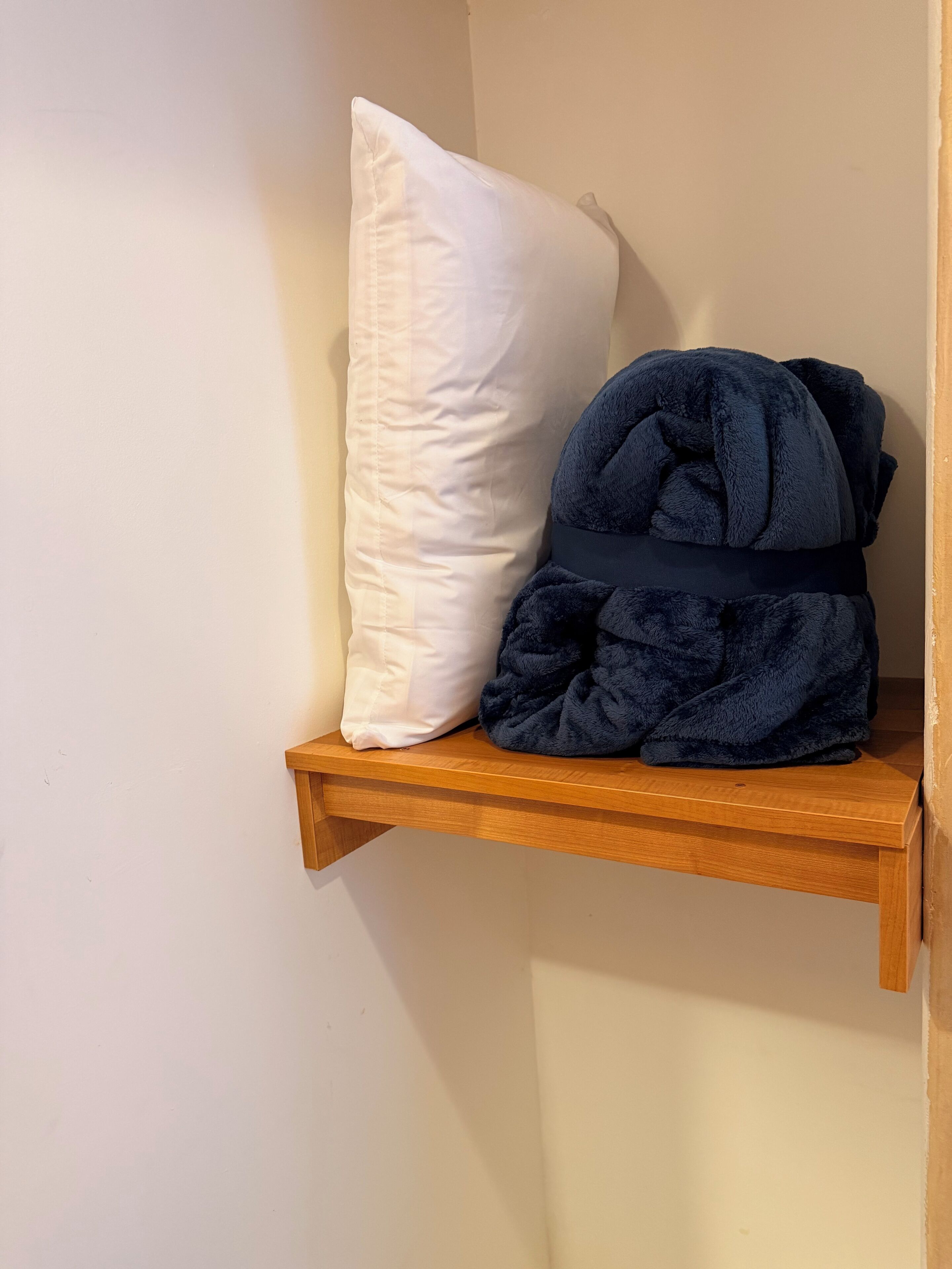 Une étagère en bois avec un coussin blanc et une couverture bleu foncé enroulée.