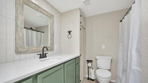 Une salle de bain avec un lavabo blanc, des meubles verts, des toilettes blanches et un rideau de douche.