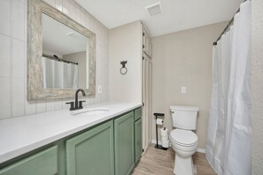 Ein Badezimmer mit einem weißen Waschbecken, grünen Schränken, einer weißen Toilette und einer Duschvorhang.