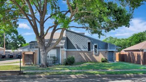 Une maison d’habitation avec un grand arbre devant, un garage et une pelouse bien entretenue.