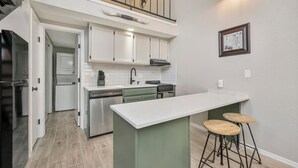 Une cuisine dotée d’un îlot central, de tabourets de bar et d’un escalier menant à un niveau supérieur.