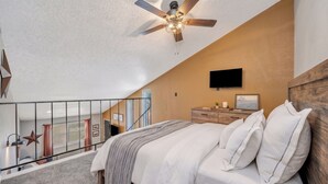 Une chambre à coucher avec un lit, un ventilateur de plafond, une télévision et un escalier menant à un étage supérieur.