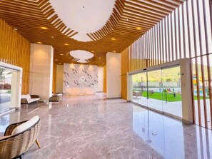 Eine geräumige Lobby mit einer Marmorrezeption, modernem Holzzellentragwerk und großen Glasüren, die zu einem Außenbereich führen.