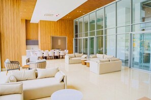 Eine geräumige Lobby mit modernem Design, ausgestattet mit einer großzügigen Sitzecke mit Sofas und Sesseln, einer Küchenzeile und großen Glasfenstern.