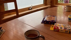 Una mesa de madera con una taza, un juego de mesa y una ventana con vistas a un lago y árboles.