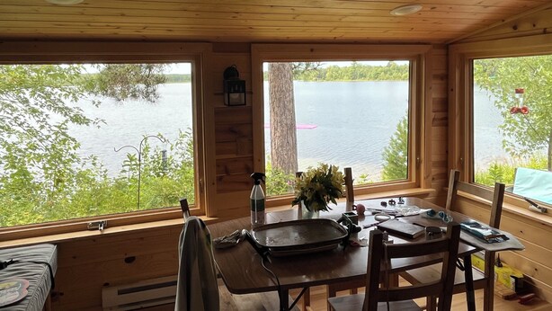 Una cabaña con una mesa de comedor, sillas, un ventanal con vista a un lago y techo de madera.