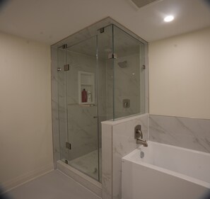 Ein modernes Badezimmer mit einer gläsernen Duschkabine, einer Marmorbadewanne und einem weißen Waschtisch.