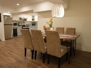 Eine moderne Küche mit integrierten Geräten, ein Essbereich mit einem Holztisch und Stühlen sowie eine Pendelleuchte.