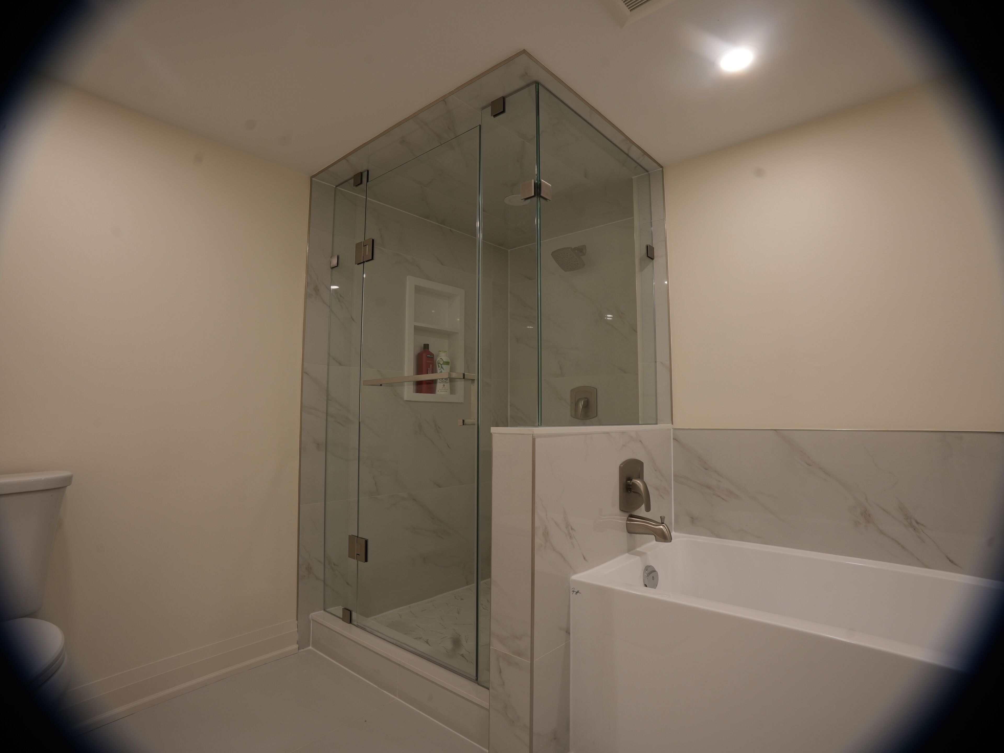 A modern bathroom with a glass-enclosed shower, a white bathtub, and a toilet.