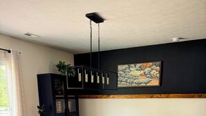 Un comedor con una mesa negra y sillas naranjas, un tapete estampado y un cuadro en la pared.