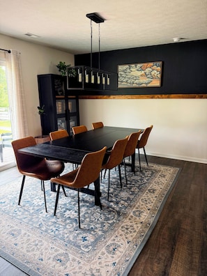 A dining area with a black table and orange chairs, a patterned rug, and a painting on the wall.