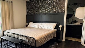 Un dormitorio con cama, mesita de noche, banco y ventilador de techo.