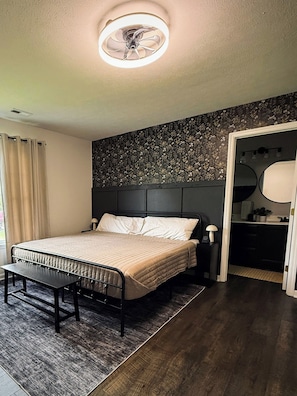A bedroom with a bed, bedside table, bench, and a ceiling fan.