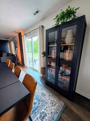 Uma sala de jantar moderna com uma mesa de madeira escura, cadeiras de couro marrom, um tapete estampado e um armário escuro com portas de vidro.
