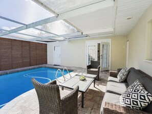 Ein überdachter Außenbereich mit Pool, Korbmöbeln und einer Tür zu einem anderen Raum.