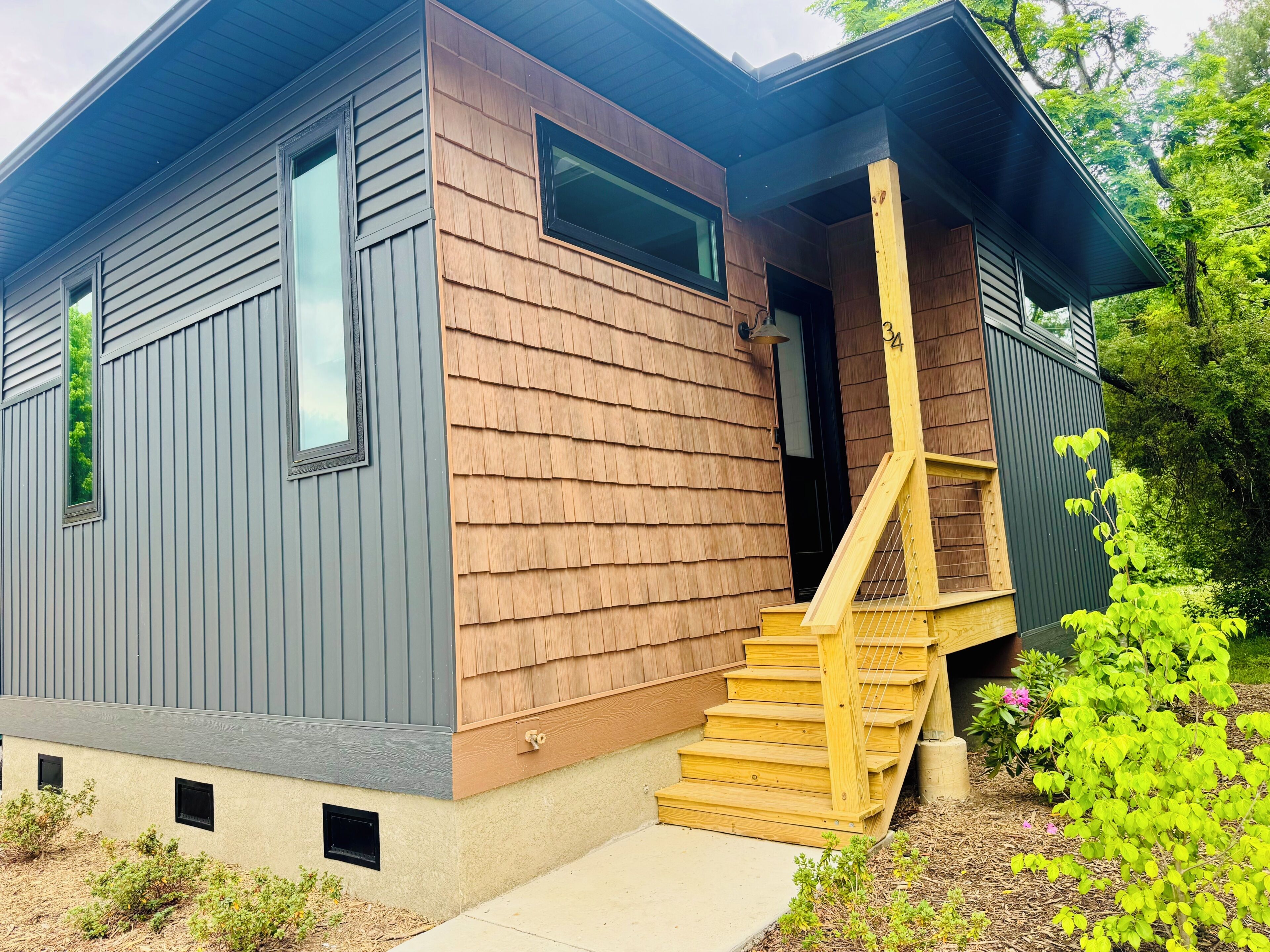 Une maison moderne à deux étages, avec une façade en bois, un porche à l’avant et un escalier menant à l’entrée.