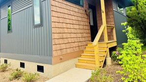 A modern two-story house with a wooden exterior, a front porch, and a staircase leading to the entrance.