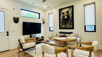 Un salon moderne avec un téléviseur à écran plat, des meubles en bois, un ventilateur de plafond et un tableau représentant un ours.