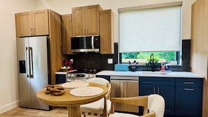 A modern kitchen with wooden cabinets, stainless steel appliances, a round wooden table, and a window with a view.