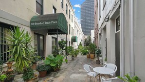 A narrow alley with potted plants, a cafe named '300 Board of Trade Place,' and white wicker furniture.