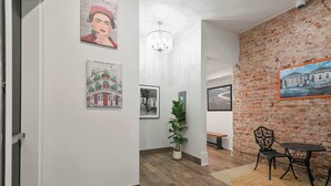 A hallway with a brick wall, wooden flooring, a chandelier, and framed artwork.