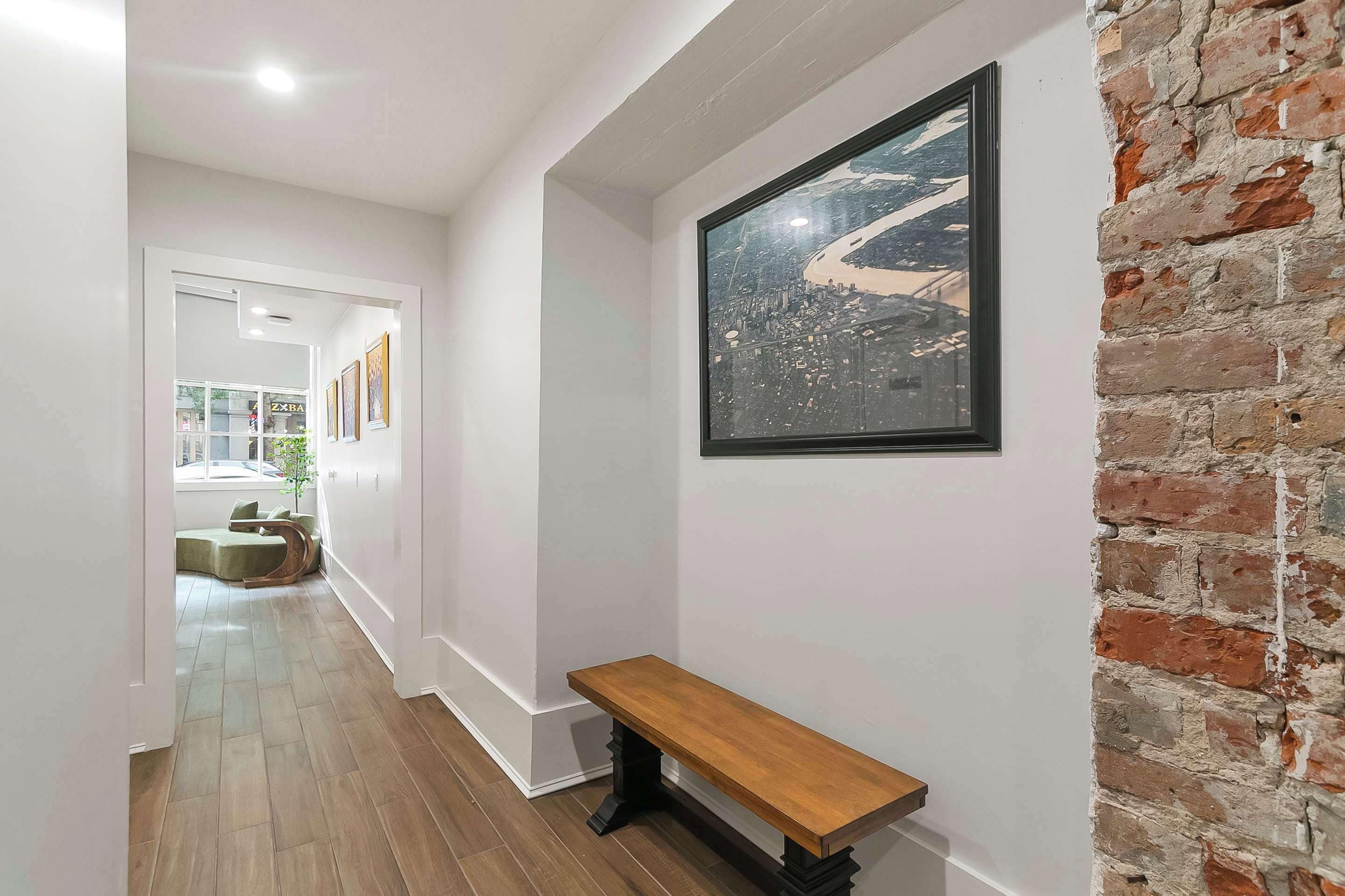 A hallway with a wooden bench, a framed cityscape artwork, and a brick wall.