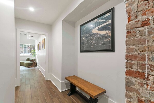 A hallway with a wooden bench, a framed cityscape artwork, and a brick wall.