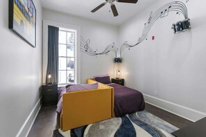 Playful Brass Band Room featuring twin beds, flowing music-note wall art, and vibrant artwork by Kerri Wilkinson celebrating New Orleans music culture.