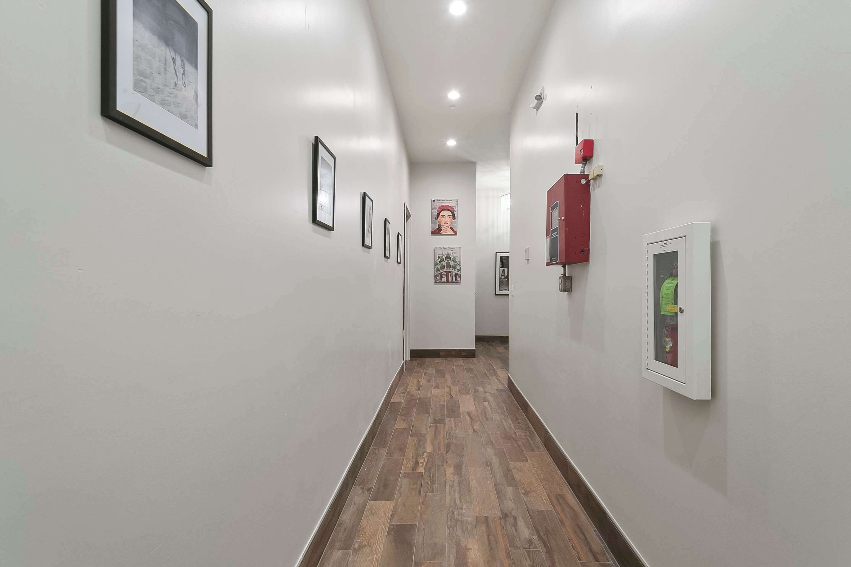 Un couloir avec des tableaux encadrés accrochés aux murs, un détecteur d’incendie et un thermostat.